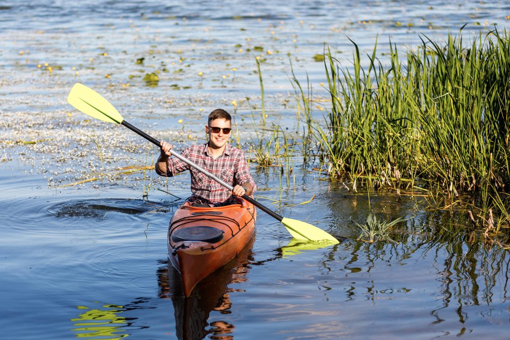 A Young Caucasian Man Sits In A Kayak And Paddles.