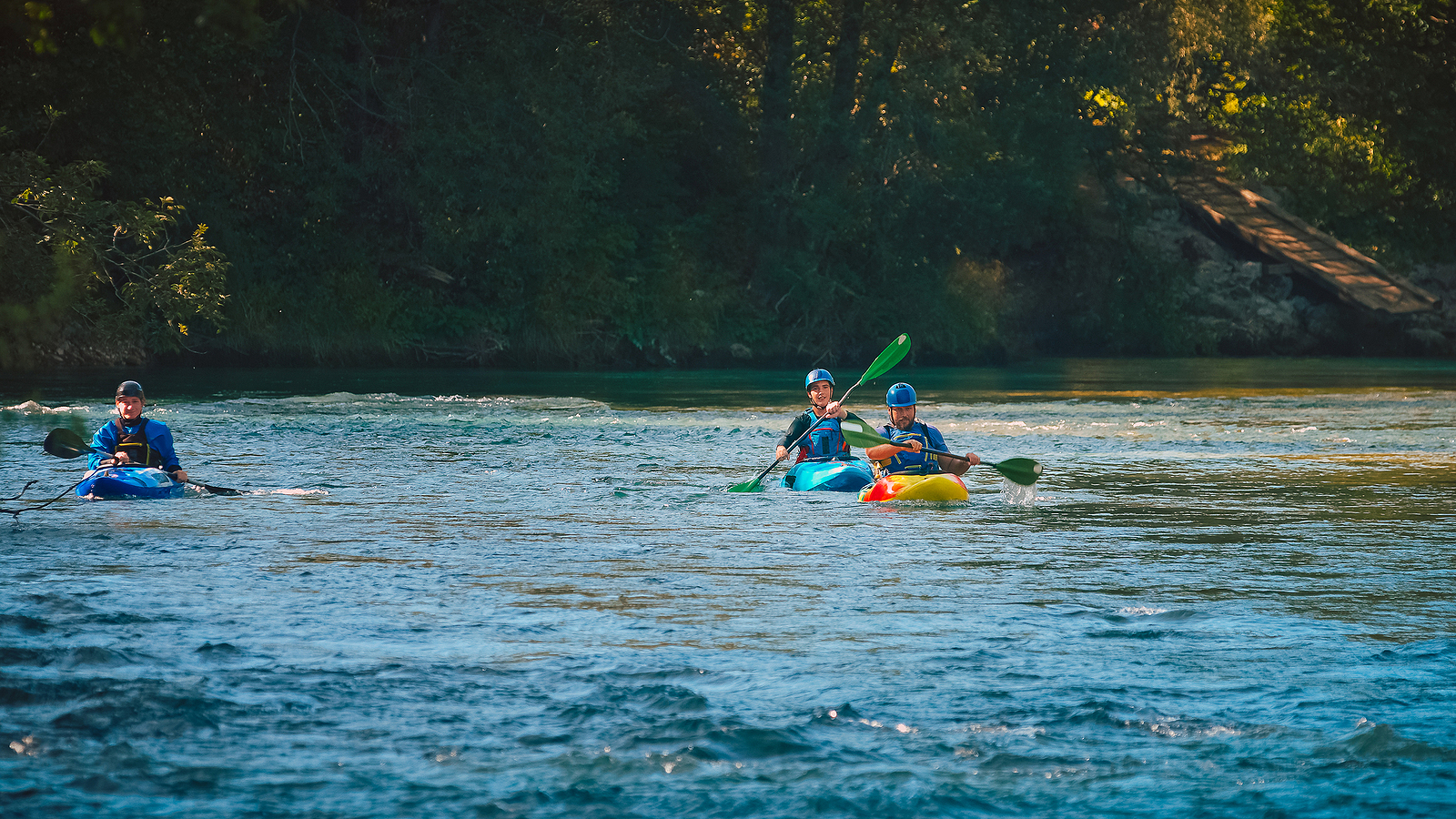 Three Kayakers Paddling And Maneuvering On The Fast-moving River